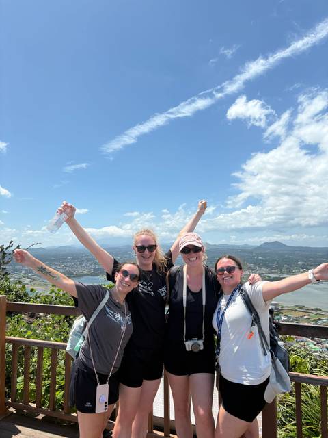 Four women posing with arms raised on a scenic overlook.