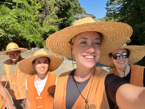 Women wearing straw hats posing for a selfie in a sunny outdoor setting.