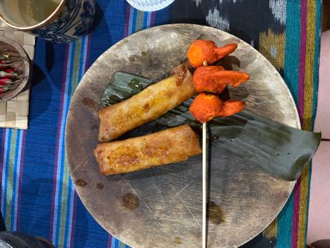 A close-up of various foods including skewered chicken and spring rolls on a table.