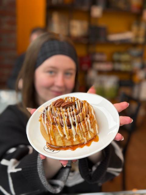       A woman holding a plate with a dessert topped with caramel and a pecan.
  