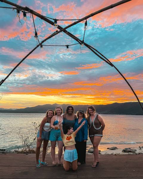       A group of people posing under a wooden arch with a colorful sunset sky.
  
