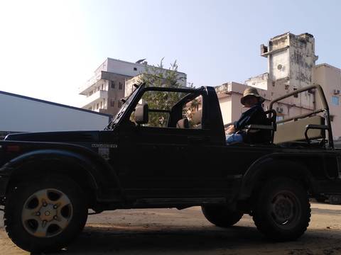 Person sitting in an open-top Jeep in an urban area.
