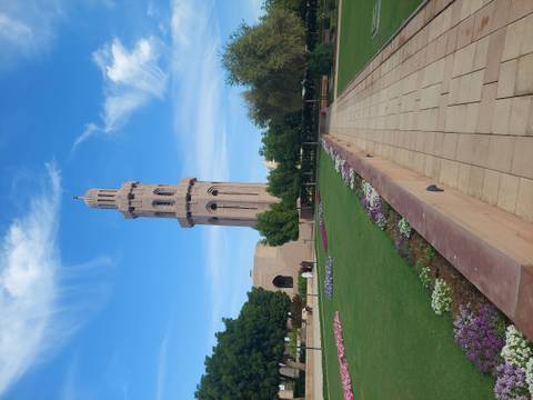       A tall minaret surrounded by gardens under a clear blue sky.
  