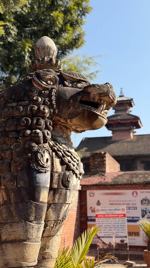       Close-up of a lion statue with traditional architecture in the background.
  