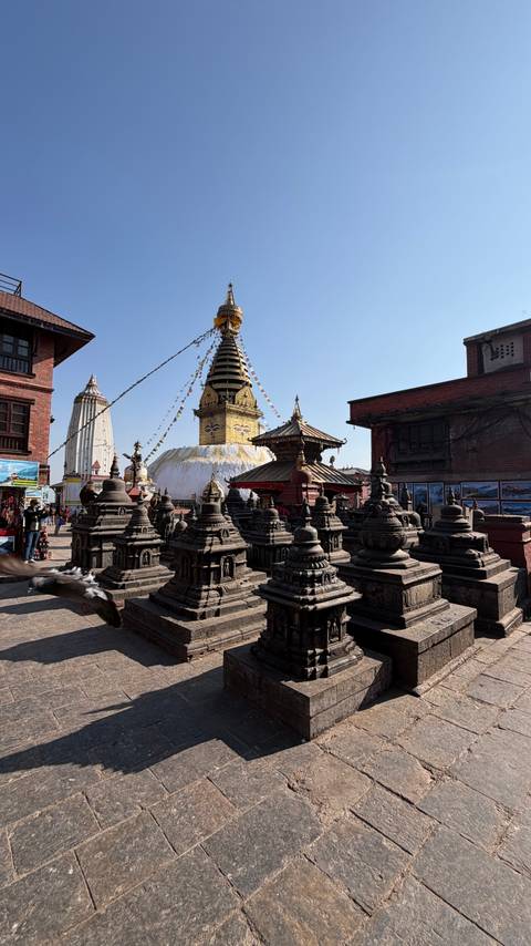       Buddhist stupas and temple structures with prayer flags and blue sky.
  