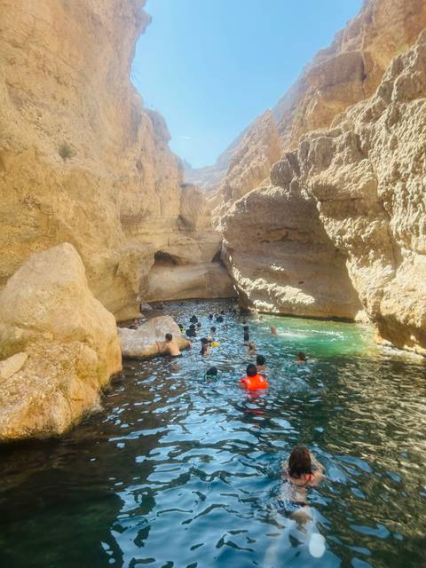 People swimming in a narrow canyon with clear water surrounded by rocky cliffs.
