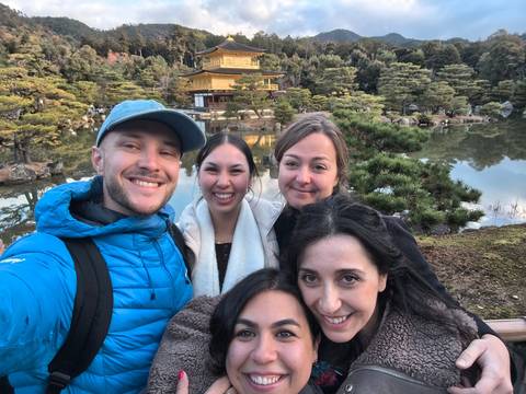 Group of friends smiling in front of a pond and traditional architecture.