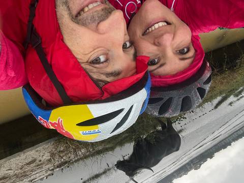 Close-up of two people cycling in rainy weather near a river.