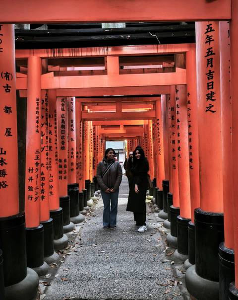 Two people standing under traditional red torii gates with inscriptions.