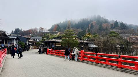 People standing on a red bridge in a scenic Japanese town.