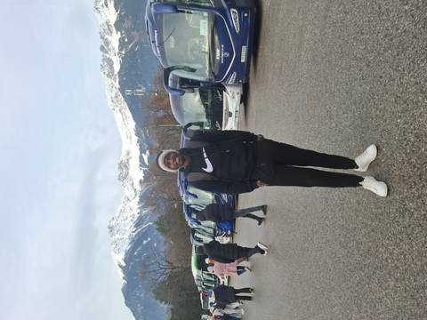 Man standing in front of a row of buses with snowy mountains in the background.