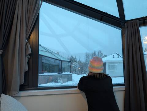 Person looking out a window at snowy surroundings.