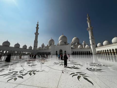       Grand mosque with multiple domes and minarets, people walking around.
  