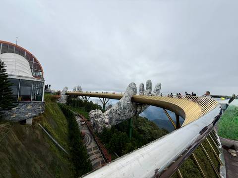       Golden bridge held by giant stone hands with tourists.
  