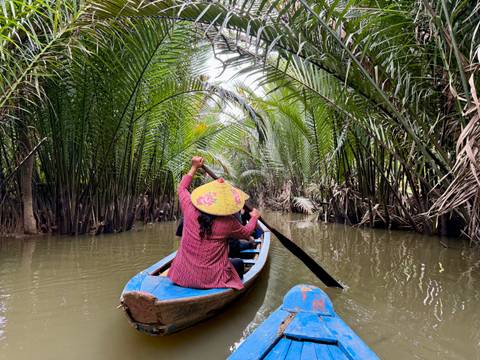       Person rowing a boat through a lush, narrow waterway.
  