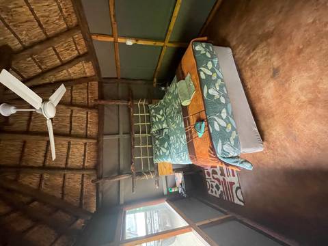       Interior of a thatched-roof hut with a bed.
  