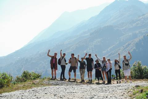      Group of people waving on a hiking trail with mountains in the background.
  