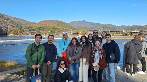       Group of people posing in front of a river with a scenic background.
  