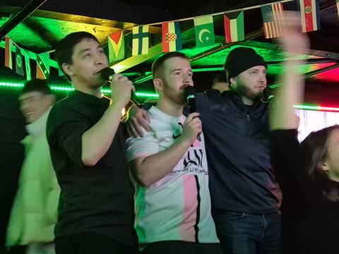 Three men singing karaoke in a bar setting.