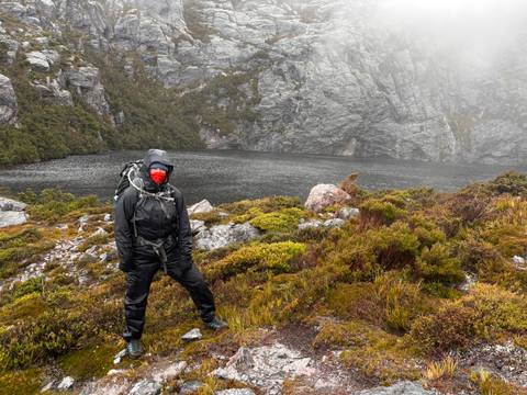 Hiker standing by a misty lake in a rocky landscape.
