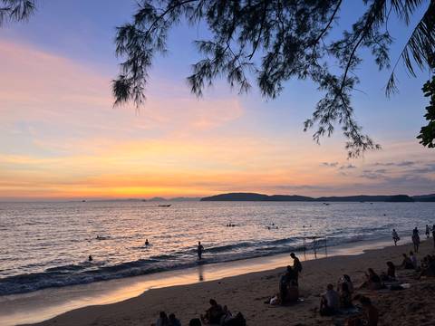      Beach during sunset with people swimming and relaxing.
  