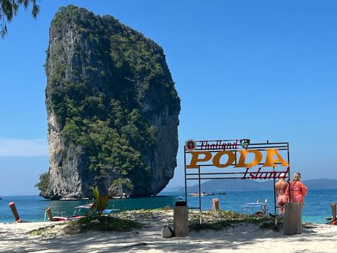       Beach with a sign for Poda Island and a rock formation.
  