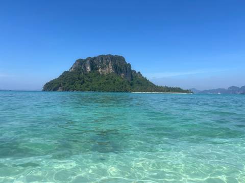       A scenic view of a lush green island surrounded by clear blue water under a clear sky.
  