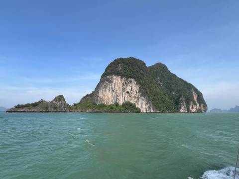       A large rocky island with greenery surrounded by ocean under a clear blue sky.
  