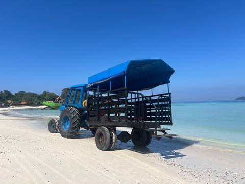       A tractor with a canopy parked on a sandy beach, with the ocean and trees in the background.
  