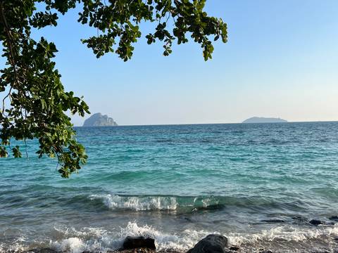       View of the ocean with islands in the distance and tree branches framing the scene.
  