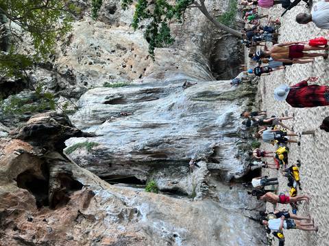       People rock climbing on a beach with large rocky cliffs.
  
