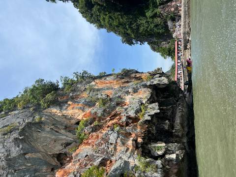       Boats and tourists in front of a large rocky cliff with orange and grey tones.
  