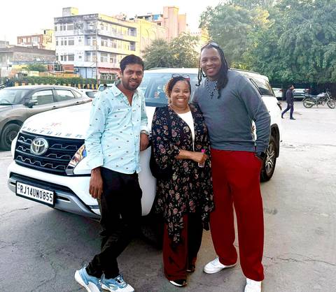 Three people standing in front of a car in an urban setting.