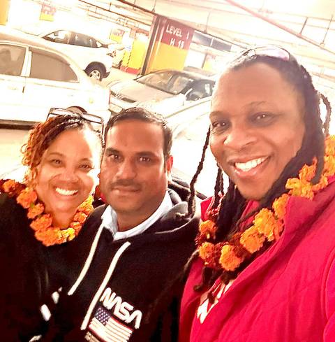       Close-up of three people wearing marigold garlands, smiling at the camera.
  
