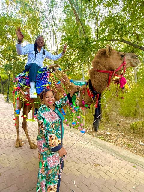 Two individuals with a camel decorated with vibrant accessories.