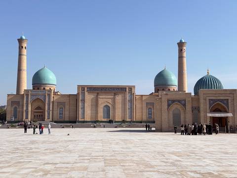 A large historical building with domes and minarets, people walking in front during the day.