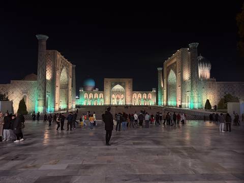 An illuminated architectural complex at night with people.
