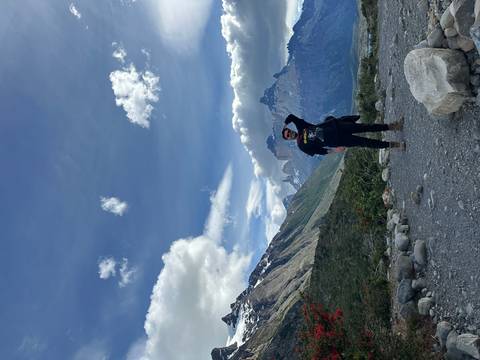       A person standing on rocky terrain with mountains in the background.
  