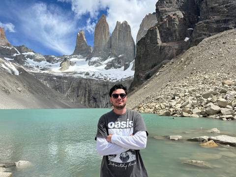       A person standing by a lake with snowy mountains.
  
