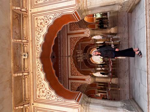 Person standing inside an ornately decorated interior with arches.
