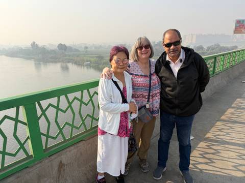 Three people posing on a bridge overlooking a river.