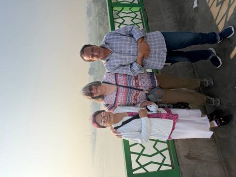       Two women posing with a man beside a river view.
  