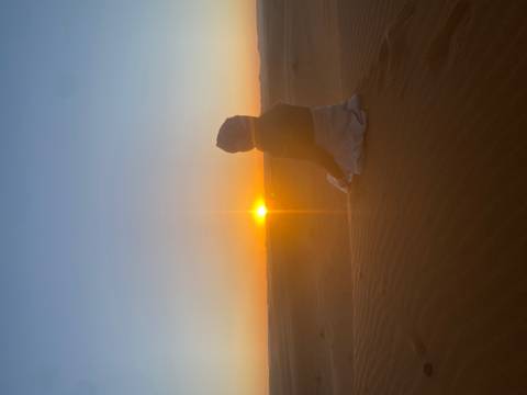 Silhouetted person sitting on a sand dune at sunset