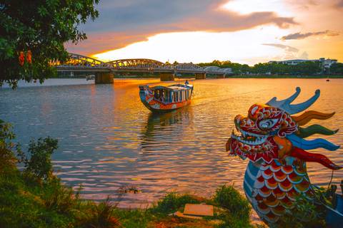       Dragon boat on a river with a bridge and sunset sky.
  