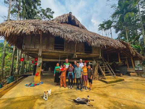       Group of people posing in front of a traditional house with a thatched roof.
  