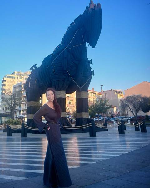 A person standing next to a wooden horse statue in a square.