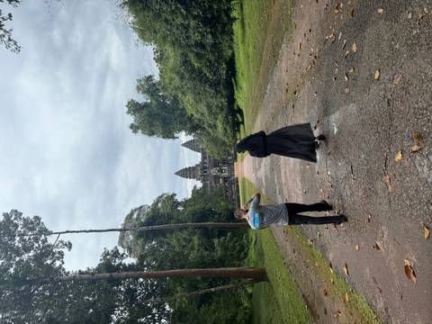 Two people walking towards a monumental temple in the jungle.