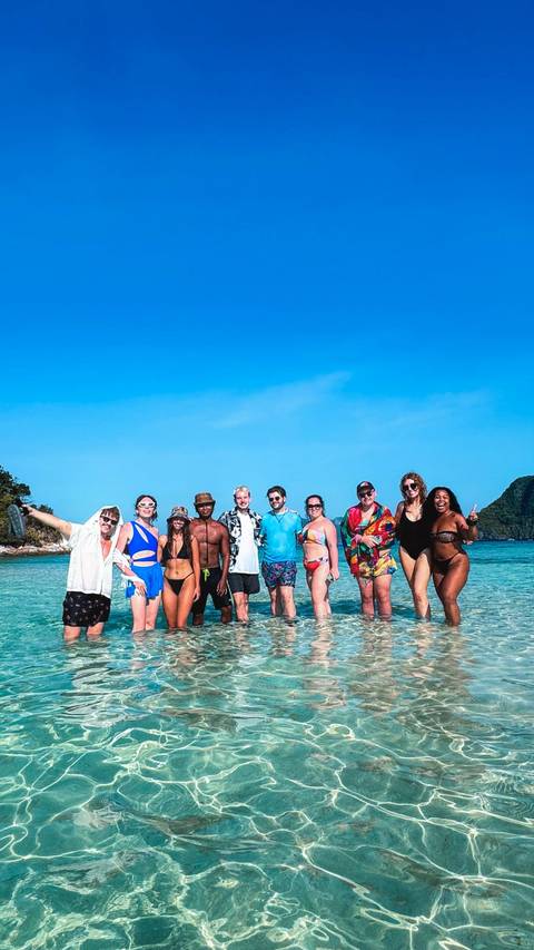 Group of people standing in shallow ocean water with distant islands visible.
