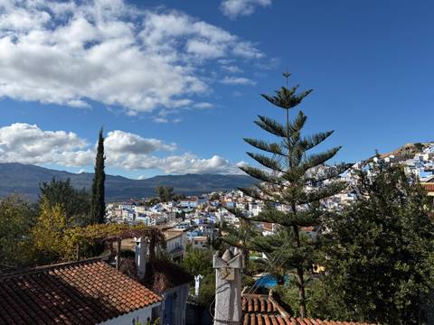       View of Chefchaouen city against a backdrop of mountains and blue sky.
  