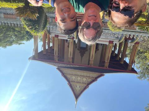 Three people posing in front of a temple with ornate architecture and blue sky.